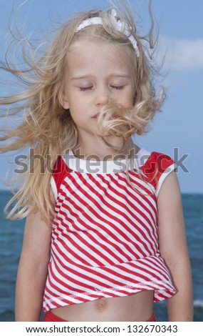 Girl with disheveled hair in the wind at the beach on a sunny day, close up against the sky and the sea