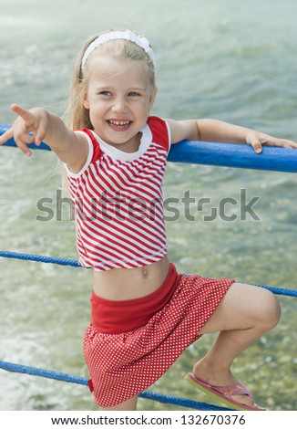 Cheerful girl with disheveled hair in the wind jumps, moves, the move to point the finger at the beach on a sunny day on the background of the surf, waves, sea and sky