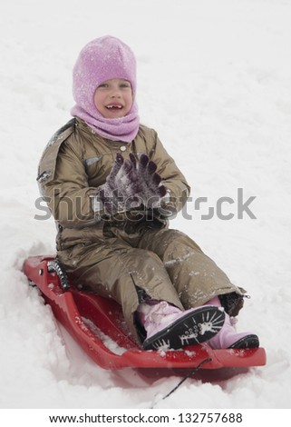 Cheerful girl of six years with no teeth in the winter sleigh rides in the snow