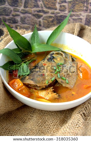 Fish curry with tomato and brinjal. Served in white bowl with ingredient background.