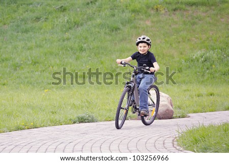 Smiling boy cycling in park against green hill