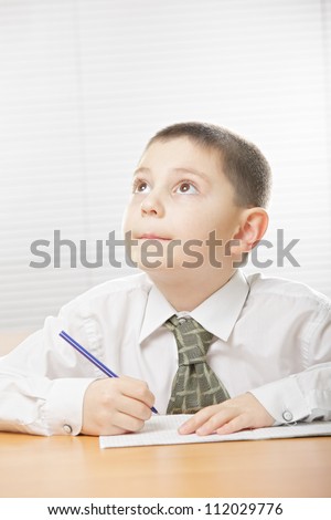 Boy in white shirt sitting at desk with copybook and looking up