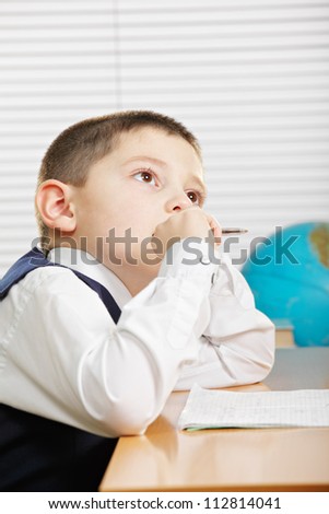 Schoolboy in white shirt sitting at desk with copybook and looking up side view