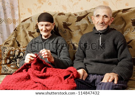 Senior couple sitting on sofa woman knitting while man looking sideways