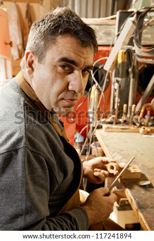 Smoking pipe maker sitting with file at workbench in workshop