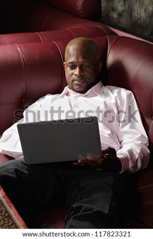 African guy in pink shirt with laptop laying down on sofa