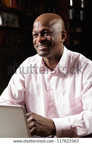 Smiling african man in pink shirt working at laptop and looking sideways