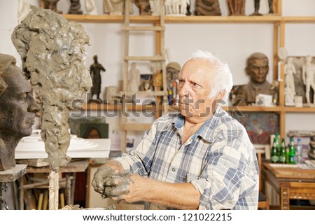 Elderly sculptor making sculpture putting clay on wire skeleton
