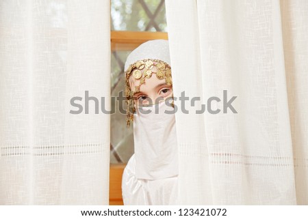 Little caucasian girl covering face hiding behind curtains