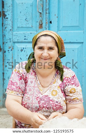 Smiling senior woman with mass of wool sitting outdoors against door