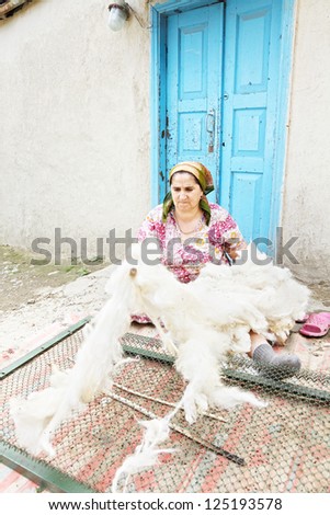 Senior woman loosening wool beating it with stick while sitting in backyard against old door