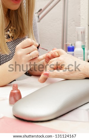 Blonde manicurist polishing fingernails of senior woman