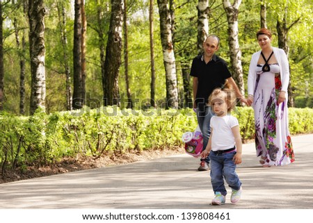 Little girl walking by the park road with parents holding hands going behind