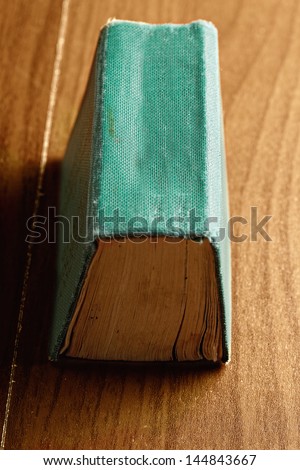 Green book spine up over wooden surface