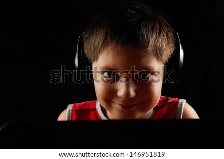 Smiling boy in headphones behind laptop closeup photo
