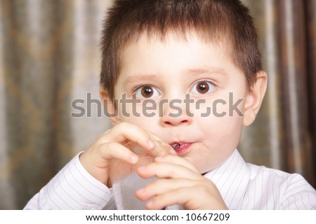 Boy in white shirt drinking juice with eyes wide open