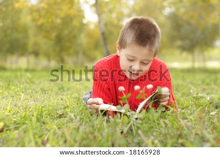 Boy in red jacket laying on grass and reading book