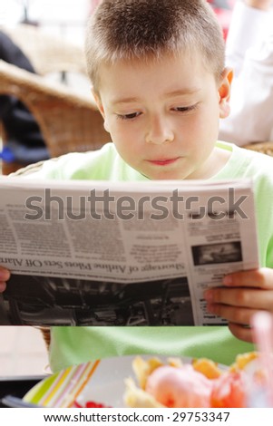 Boy in green reading newspaper at the table in outdoor cafe
