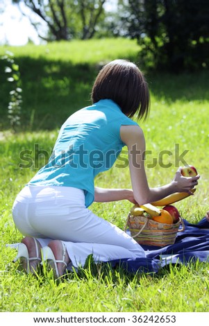 stock photo Young woman bending over basket with fruits outdoors