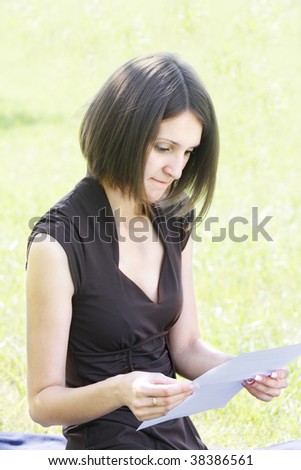 Pretty young woman in brown dress reading letter outdoors