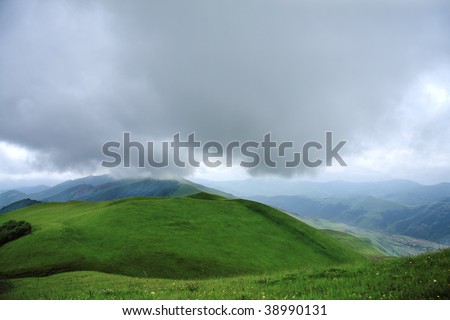 Big rain cloud hanging over green hill in Caucasus mountains