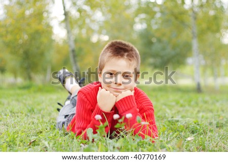 Smiling boy in red jacket laying down on green grass