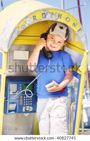 Little smiling boy in blue shirt at old rusty pay-phone