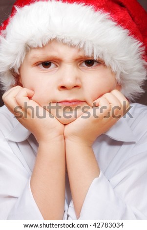 Little boy in Santa cap with angry facial expression