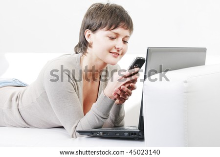 Pretty young woman reading message on mobile phone while laying on sofa