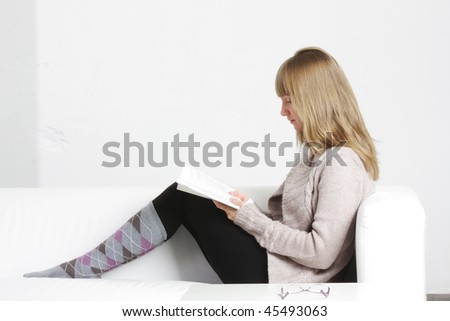 Young blonde woman reading book sitting on sofa side-view