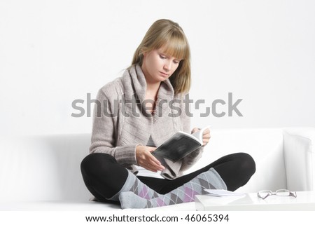 Young blonde woman reading book on sofa with white table on foreground
