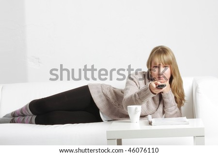Young blonde woman laying down on sofa with remote control