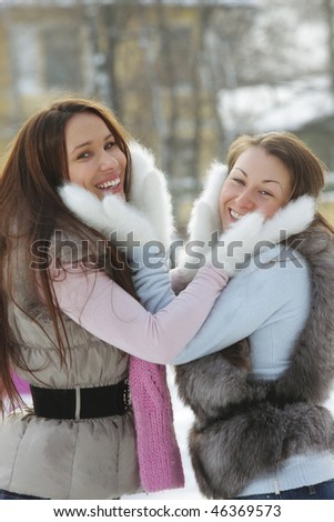 Two young positive women in white fur mittens outdoors