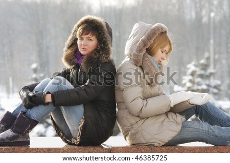 Two young woman sitting on stone parapet have serious talk