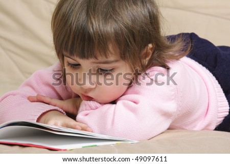 Little girl in pink sweater reading book on sofa closeup photo