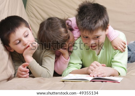 Three children reading book laying on brown sofa