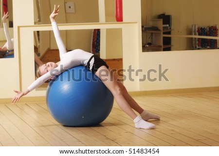 Little gymnast girl laying down on big blue ball in gym