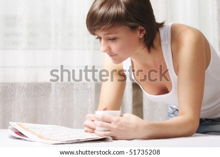 Young woman with cup reading paper leaning on table