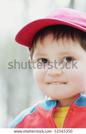 Little boy in red cap biting lip closeup outdoor photo