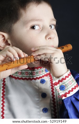 Little boy in blue playing wooden flute against dark background