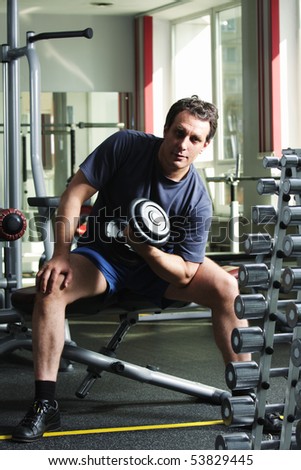 Man in shirt and shorts training biceps with dumb-bell at gym