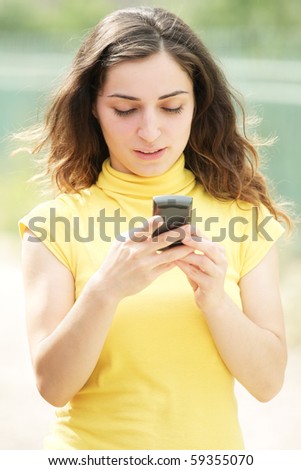 Young brunette woman in yellow shirt reading message on cellphone