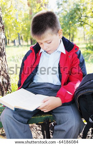Kid in red jacket reading book in autumn park