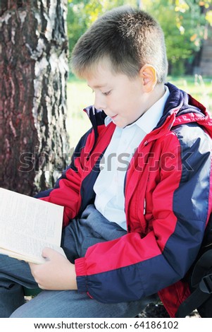 Kid in red jacket reading book in autumn park side-view