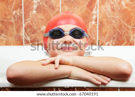 Funny boy in swimming goggles and cap leaning on bath edge