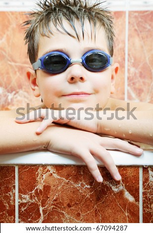 Cute boy in blue swimming goggles leaning on bath edge