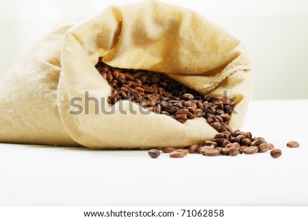 Roasted coffee scattered from textile bag over light background