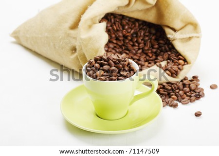 Green cup with coffee beans over light background