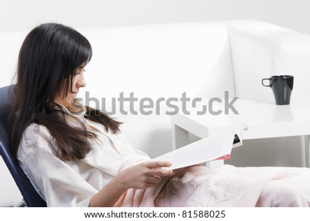 Brunette woman in chair reading magazine sideview