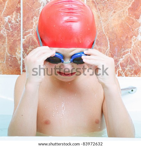 Little boy in rubber cap taking off goggles at bathtub